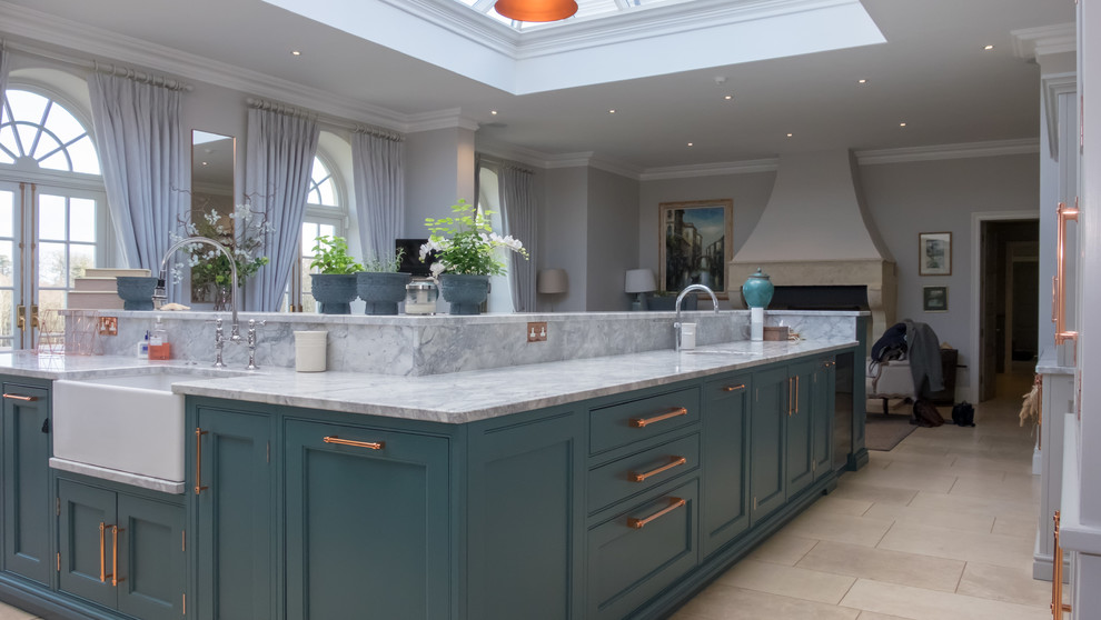 Inspiration for an expansive transitional l-shaped open plan kitchen in Berkshire with a farmhouse sink, shaker cabinets, grey cabinets, granite benchtops, grey splashback, stone slab splashback, stainless steel appliances, limestone floors, multiple islands, beige floor and grey benchtop.