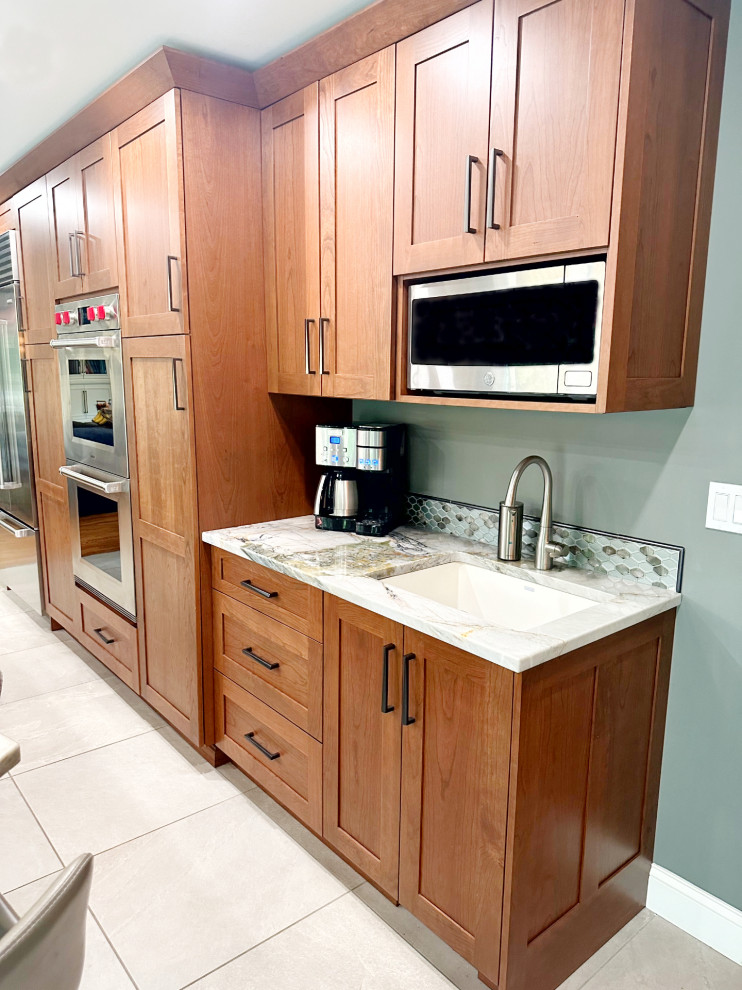 Eat-in kitchen - mid-sized transitional porcelain tile and gray floor eat-in kitchen idea with recessed-panel cabinets, medium tone wood cabinets, quartzite countertops, green backsplash, mosaic tile backsplash, stainless steel appliances and an island