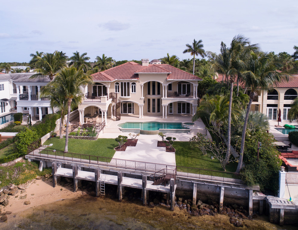 Photo of a large mediterranean two-storey stucco beige house exterior in Miami with a tile roof and a brown roof.