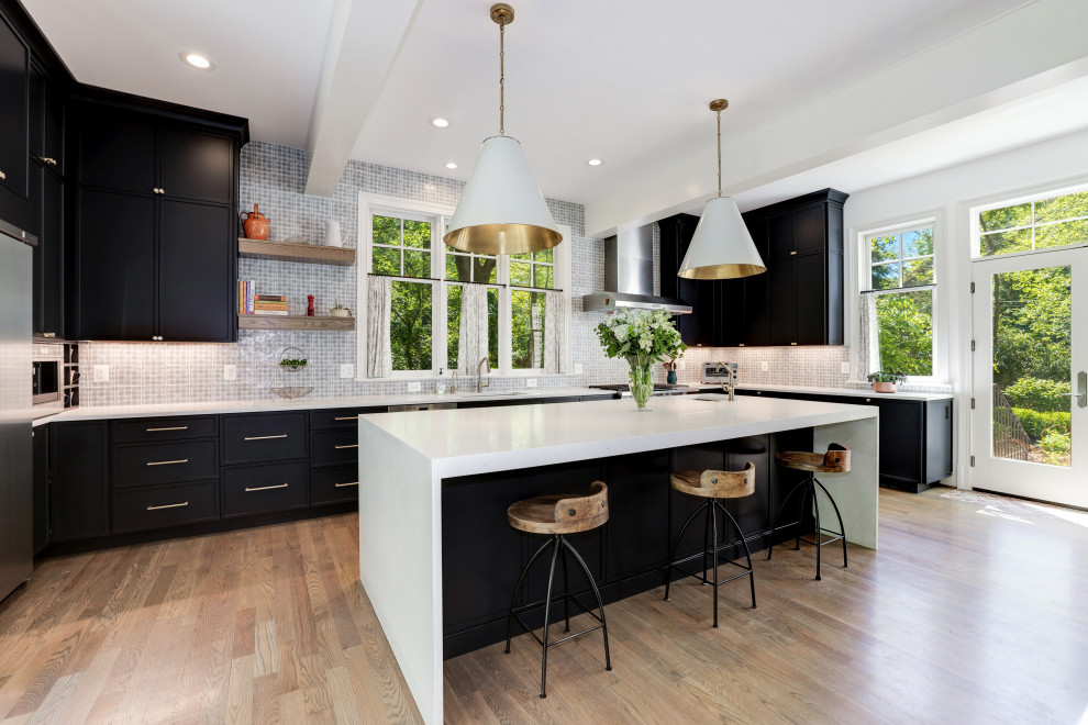 This is an example of a transitional u-shaped kitchen in Other with an undermount sink, recessed-panel cabinets, black cabinets, stainless steel appliances, medium hardwood floors, with island, brown floor and white benchtop.