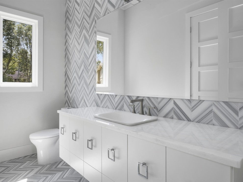 Design ideas for a large transitional powder room in Orlando with flat-panel cabinets, white cabinets, a two-piece toilet, gray tile, white tile, grey walls, a drop-in sink, grey floor and white benchtops.