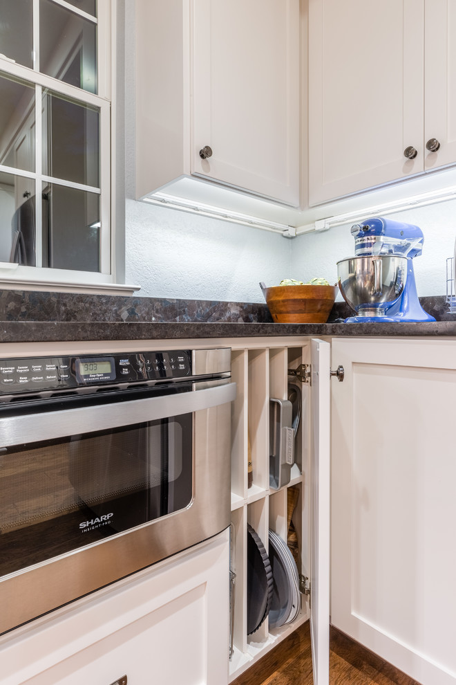 Eat-in kitchen - mid-sized transitional l-shaped medium tone wood floor eat-in kitchen idea in Austin with an undermount sink, shaker cabinets, white cabinets, granite countertops, white backsplash, ceramic backsplash, stainless steel appliances and an island