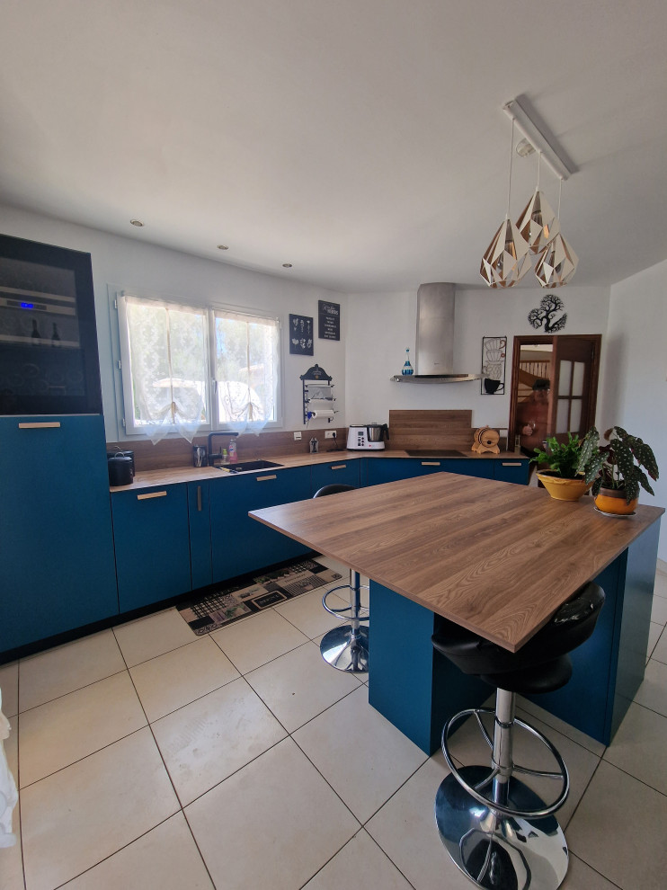 Photo of a large industrial galley separate kitchen in Toulouse with an undermount sink, beaded inset cabinets, blue cabinets, wood benchtops, brown splashback, timber splashback, panelled appliances, ceramic floors, with island, beige floor and brown benchtop.