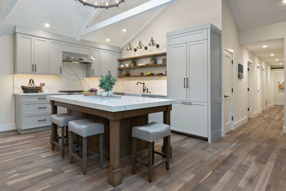 Inspiration for a transitional l-shaped dark wood floor and brown floor kitchen remodel with an undermount sink, shaker cabinets, gray cabinets, white backsplash, stone slab backsplash, paneled appliances, an island and white countertops