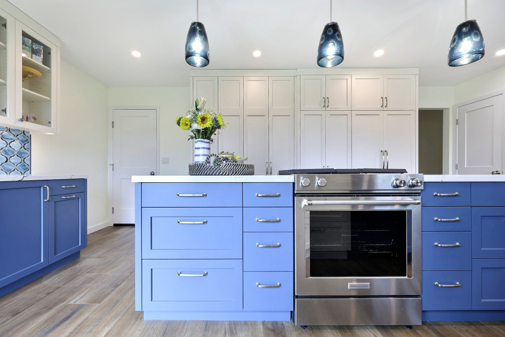 Photo of a large classic open plan kitchen in San Francisco with a double-bowl sink, shaker cabinets, blue cabinets, engineered stone countertops, blue splashback, glass tiled splashback, stainless steel appliances, medium hardwood flooring, an island, brown floors and white worktops.