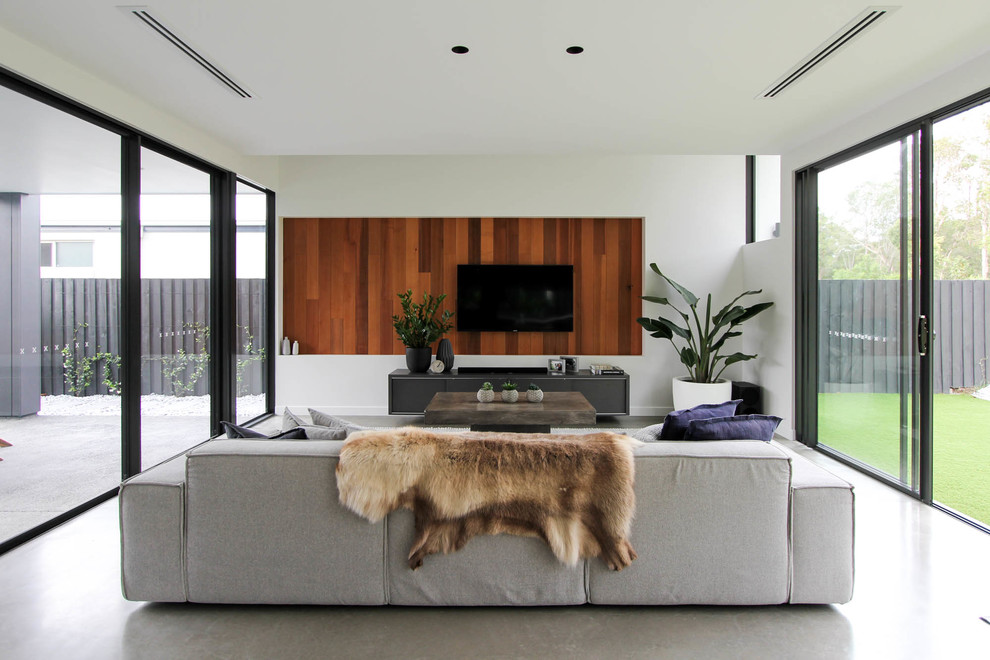 This is an example of a contemporary enclosed living room in Sunshine Coast with white walls, concrete floors, a wall-mounted tv and grey floor.