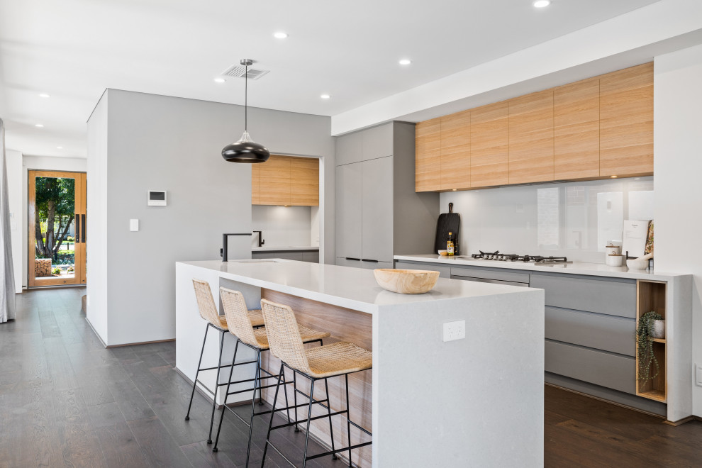 Contemporary l-shaped eat-in kitchen in Perth with an undermount sink, flat-panel cabinets, grey cabinets, white splashback, glass sheet splashback, panelled appliances, medium hardwood floors, with island, brown floor and white benchtop.