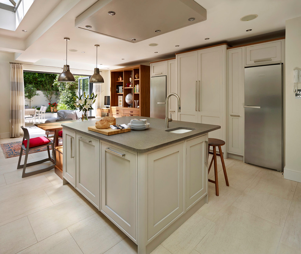 Inspiration for a mid-sized contemporary l-shaped open plan kitchen in London with shaker cabinets, stainless steel appliances, with island, a drop-in sink, grey cabinets, grey splashback, glass sheet splashback and limestone floors.