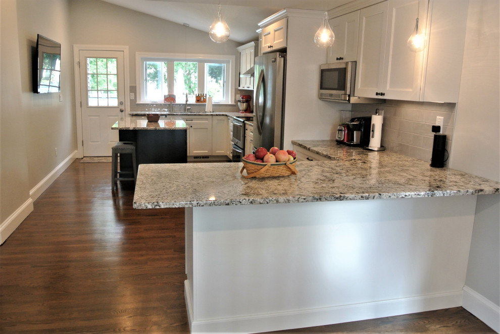 Example of a transitional l-shaped medium tone wood floor and brown floor eat-in kitchen design in Boston with an undermount sink, shaker cabinets, white cabinets, granite countertops, beige backsplash, subway tile backsplash, stainless steel appliances, an island and beige countertops
