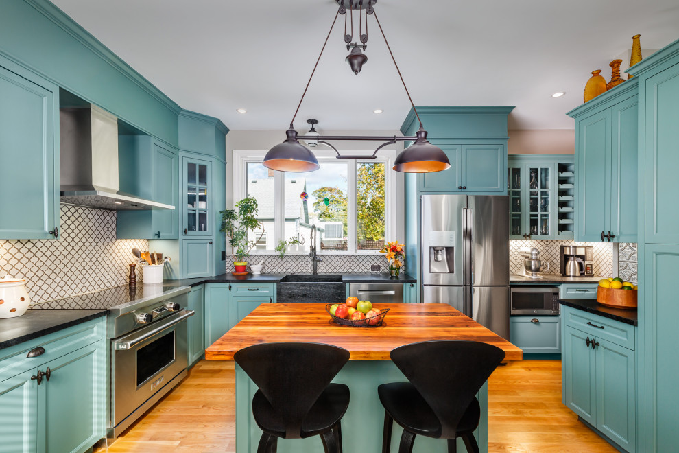 This is an example of a mid-sized traditional u-shaped separate kitchen in Boston with a farmhouse sink, recessed-panel cabinets, turquoise cabinets, soapstone benchtops, white splashback, ceramic splashback, stainless steel appliances, medium hardwood floors, with island and black benchtop.