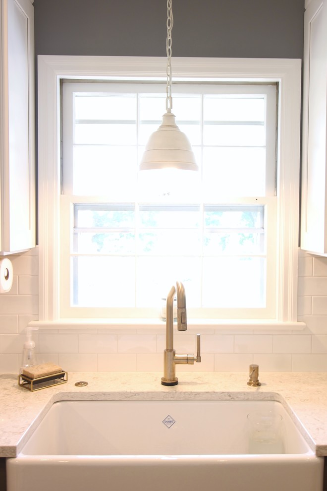 Mid-sized transitional u-shaped medium tone wood floor and brown floor enclosed kitchen photo with a farmhouse sink, shaker cabinets, white cabinets, quartz countertops, white backsplash, subway tile backsplash, white appliances, no island and beige countertops