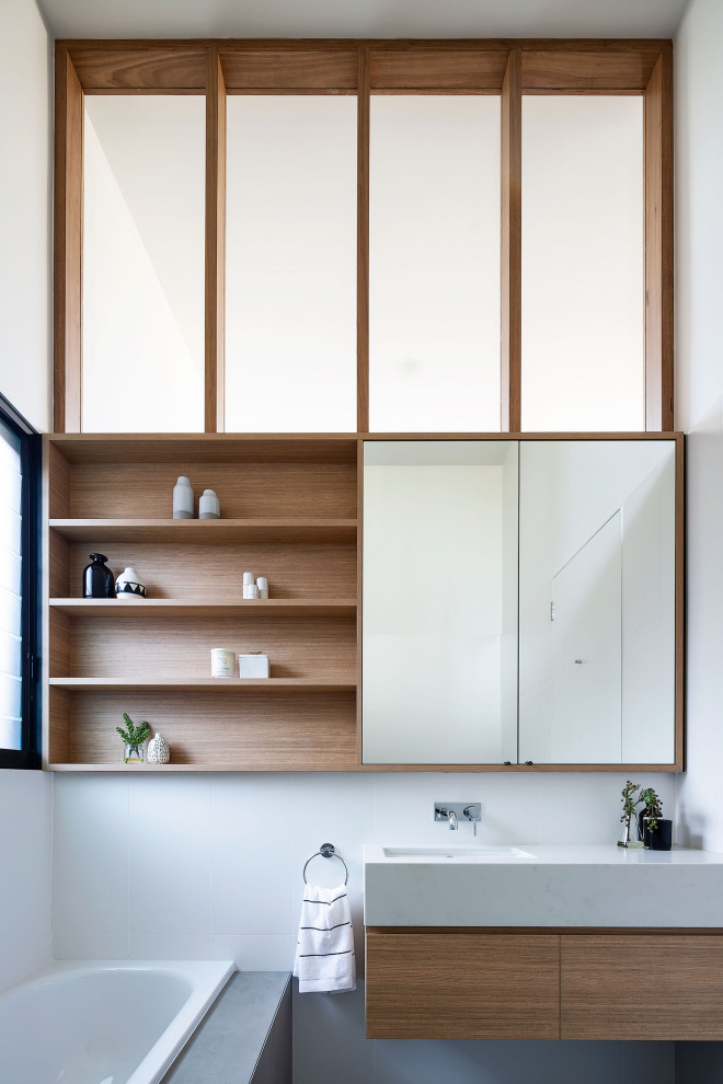 Cette image montre une salle de bain design en bois brun avec un placard à porte plane, une baignoire posée, un mur blanc, un lavabo encastré, un plan de toilette blanc, meuble simple vasque et meuble-lavabo suspendu.