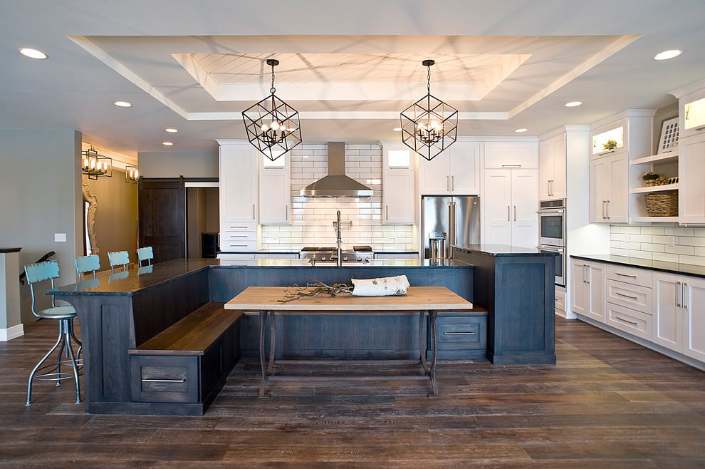 Example of a large transitional l-shaped dark wood floor and brown floor eat-in kitchen design with a farmhouse sink, raised-panel cabinets, white cabinets, quartz countertops, white backsplash, subway tile backsplash, stainless steel appliances and an island