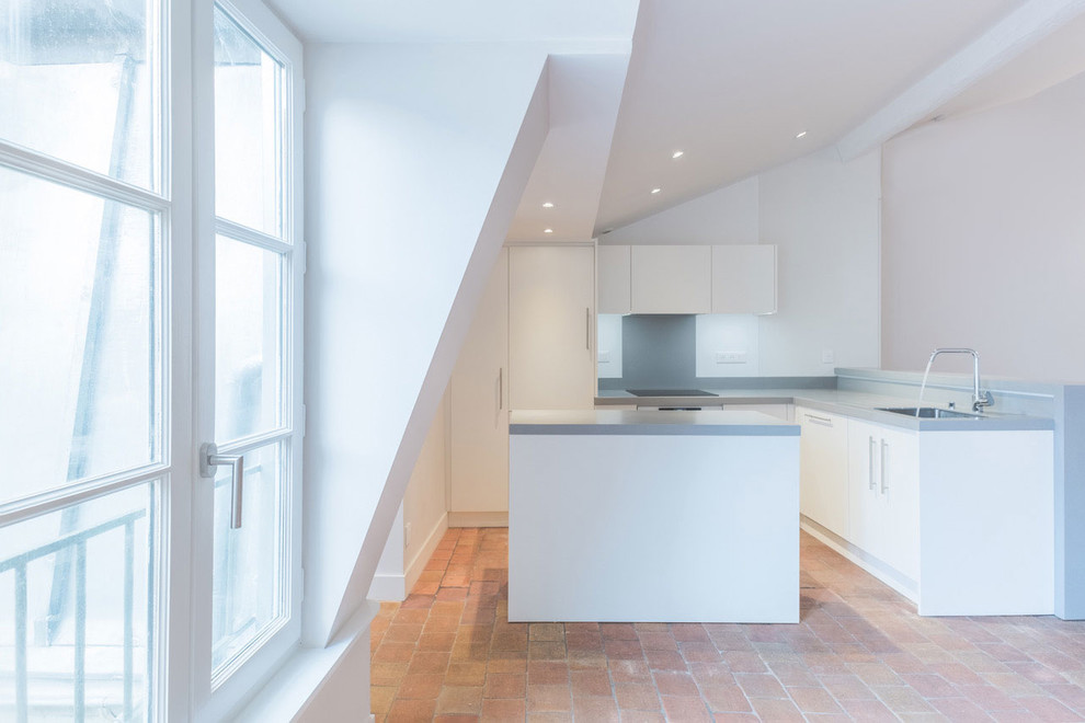 Mid-sized contemporary l-shaped open plan kitchen in Lyon with a single-bowl sink, beaded inset cabinets, white cabinets, solid surface benchtops, grey splashback, with island and red floor.