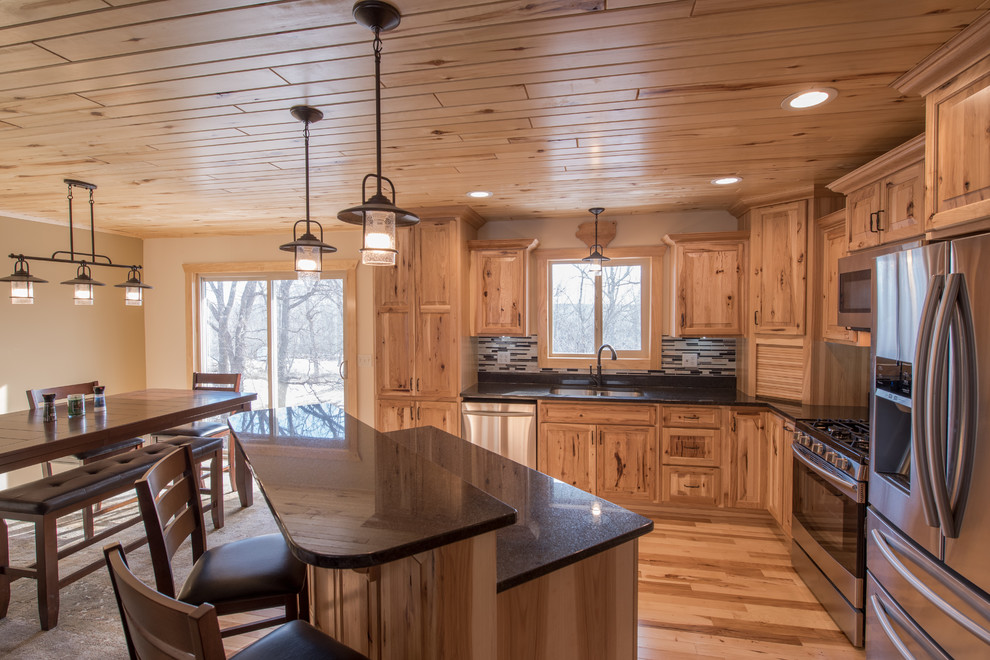 Mid-sized country l-shaped open plan kitchen in Minneapolis with a double-bowl sink, raised-panel cabinets, light wood cabinets, granite benchtops, multi-coloured splashback, matchstick tile splashback, stainless steel appliances, light hardwood floors and with island.