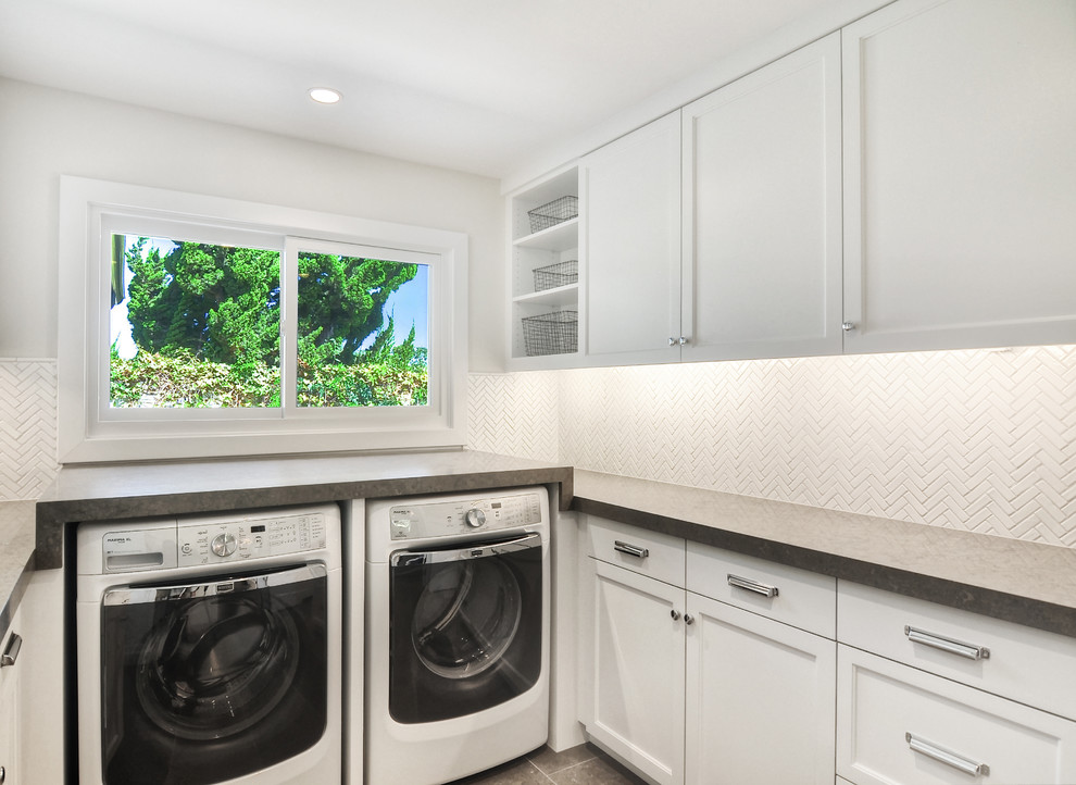 Mid-sized transitional u-shaped dedicated laundry room in Orange County with white cabinets, a side-by-side washer and dryer, white walls, grey benchtop, shaker cabinets, limestone benchtops, limestone floors and grey floor.