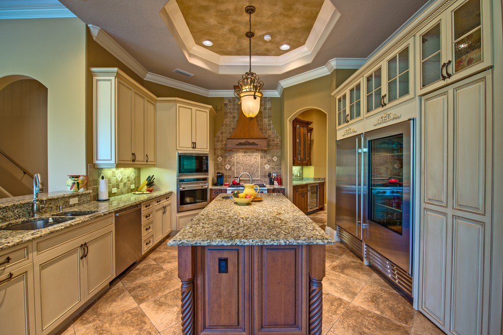 This is an example of a large mediterranean galley separate kitchen in Tampa with an undermount sink, raised-panel cabinets, beige cabinets, granite benchtops, beige splashback, ceramic splashback, stainless steel appliances, ceramic floors, with island and beige floor.