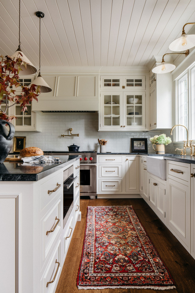 Cette photo montre une cuisine avec un évier de ferme, un placard à porte vitrée, des portes de placard blanches, une crédence blanche, îlot et un plafond en lambris de bois.