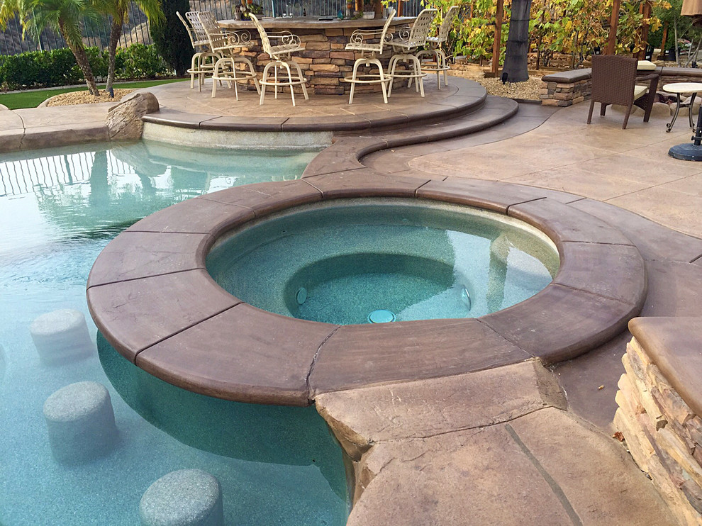 Photo of a large tropical backyard custom-shaped pool in Los Angeles with a hot tub and stamped concrete.