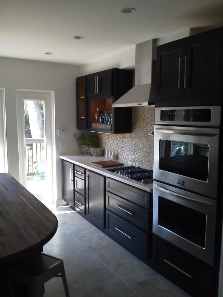 Eat-in kitchen - mid-sized transitional galley porcelain tile and gray floor eat-in kitchen idea in Miami with a double-bowl sink, shaker cabinets, black cabinets, solid surface countertops, multicolored backsplash, mosaic tile backsplash, stainless steel appliances and an island