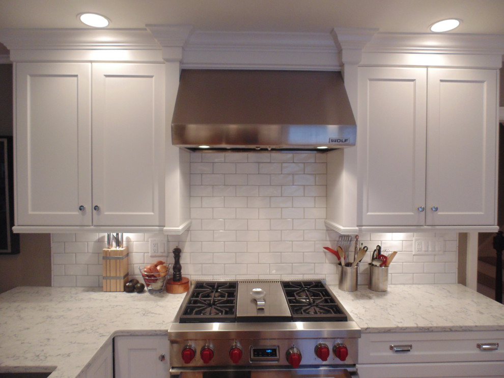 Example of a large transitional u-shaped medium tone wood floor and brown floor eat-in kitchen design with an undermount sink, recessed-panel cabinets, white cabinets, quartz countertops, white backsplash, subway tile backsplash, stainless steel appliances, an island and white countertops