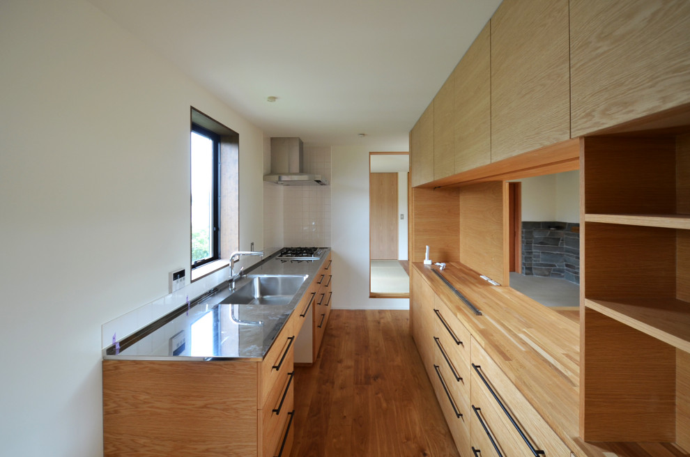 Photo of a mid-sized scandinavian single-wall separate kitchen in Other with an integrated sink, shaker cabinets, stainless steel benchtops, white splashback, porcelain splashback, stainless steel appliances, medium hardwood floors, a peninsula, brown floor, brown benchtop and timber.