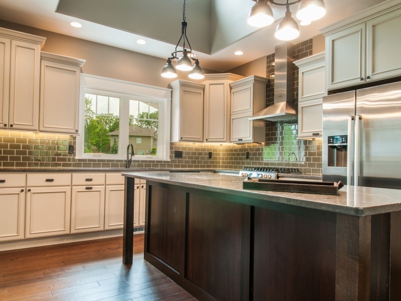 Inspiration for a large transitional l-shaped medium tone wood floor and brown floor kitchen remodel in Cedar Rapids with an undermount sink, beaded inset cabinets, white cabinets, granite countertops, gray backsplash, subway tile backsplash, stainless steel appliances and an island