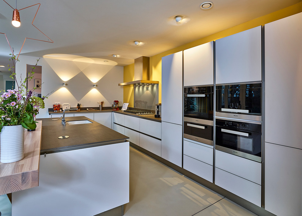 Design ideas for a large contemporary l-shaped open plan kitchen in Other with a drop-in sink, flat-panel cabinets, white cabinets, black appliances, concrete floors and with island.