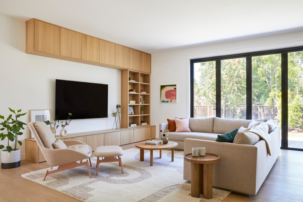Diseño de sala de estar abierta nórdica grande sin chimenea con paredes blancas, suelo de madera clara, televisor colgado en la pared y suelo marrón