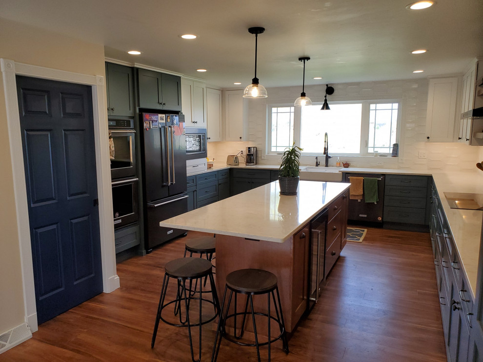 Photo of an expansive country u-shaped eat-in kitchen in Other with a farmhouse sink, flat-panel cabinets, blue cabinets, quartz benchtops, white splashback, ceramic splashback, black appliances, medium hardwood floors, with island, brown floor and white benchtop.