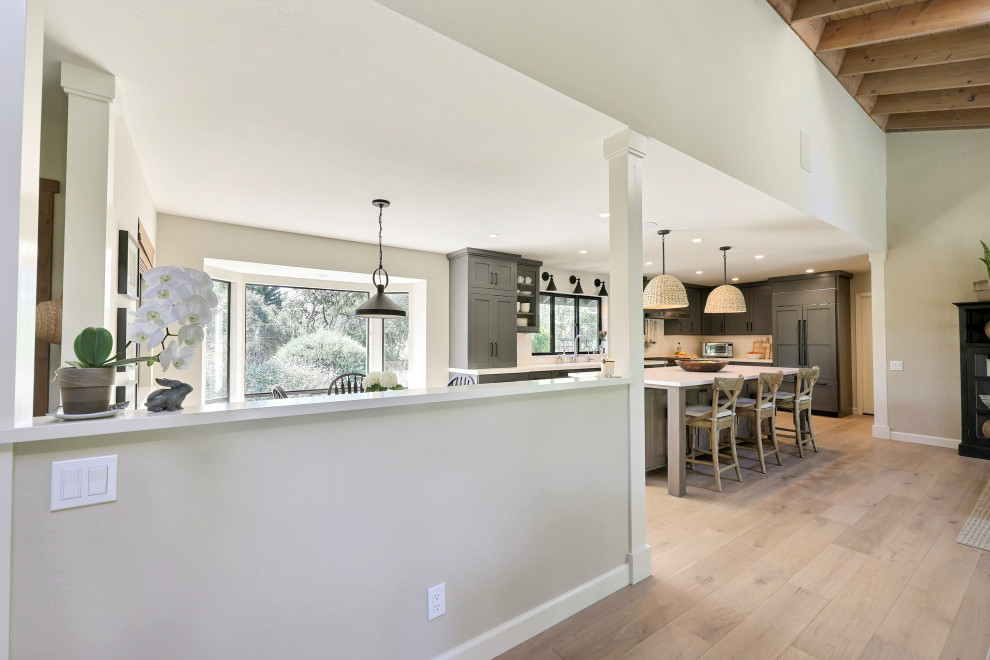 Example of a mid-sized transitional l-shaped laminate floor open concept kitchen design with a double-bowl sink, flat-panel cabinets, gray cabinets, quartz countertops, white backsplash, ceramic backsplash, stainless steel appliances, an island and white countertops