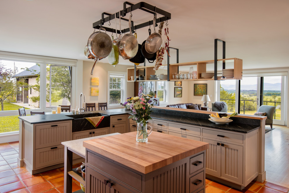 Photo of a mid-sized country open plan kitchen in Burlington with with island, a farmhouse sink, beaded inset cabinets, grey cabinets, granite benchtops, black splashback, stone slab splashback and ceramic floors.