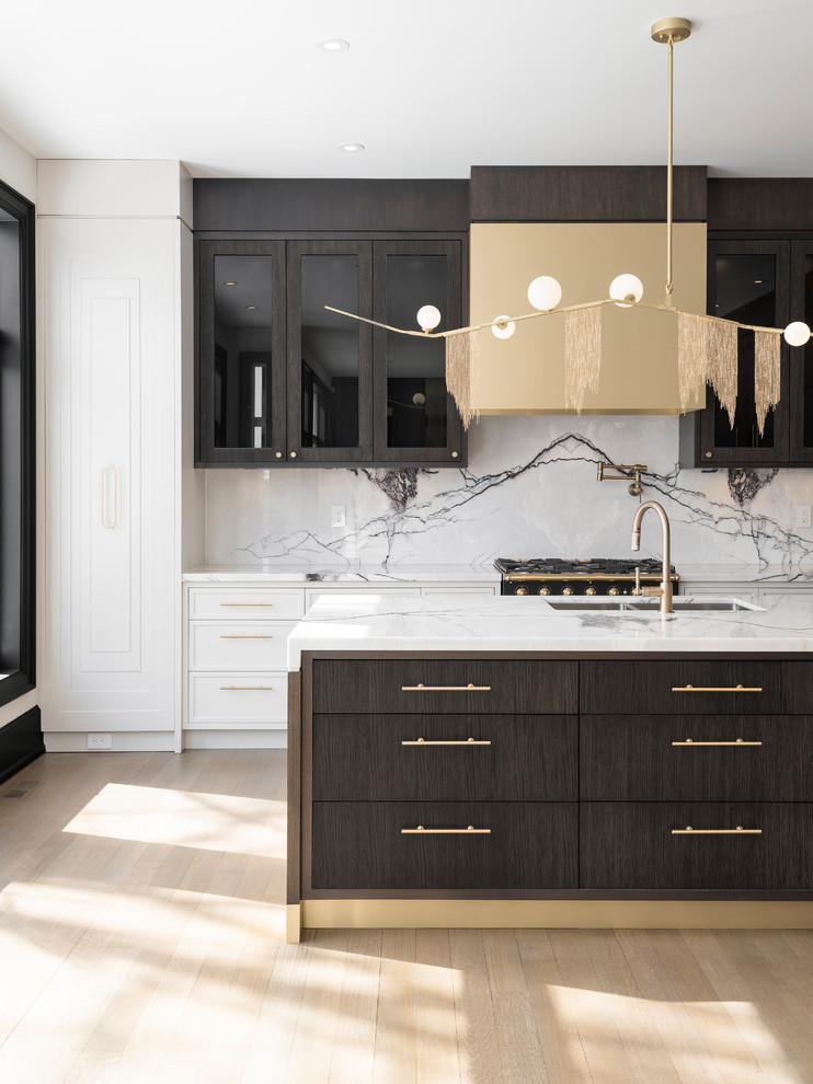 This is an example of a large contemporary kitchen in Toronto with an undermount sink, dark wood cabinets, marble benchtops, marble splashback, with island, recessed-panel cabinets, white splashback, black appliances, light hardwood floors and beige floor.