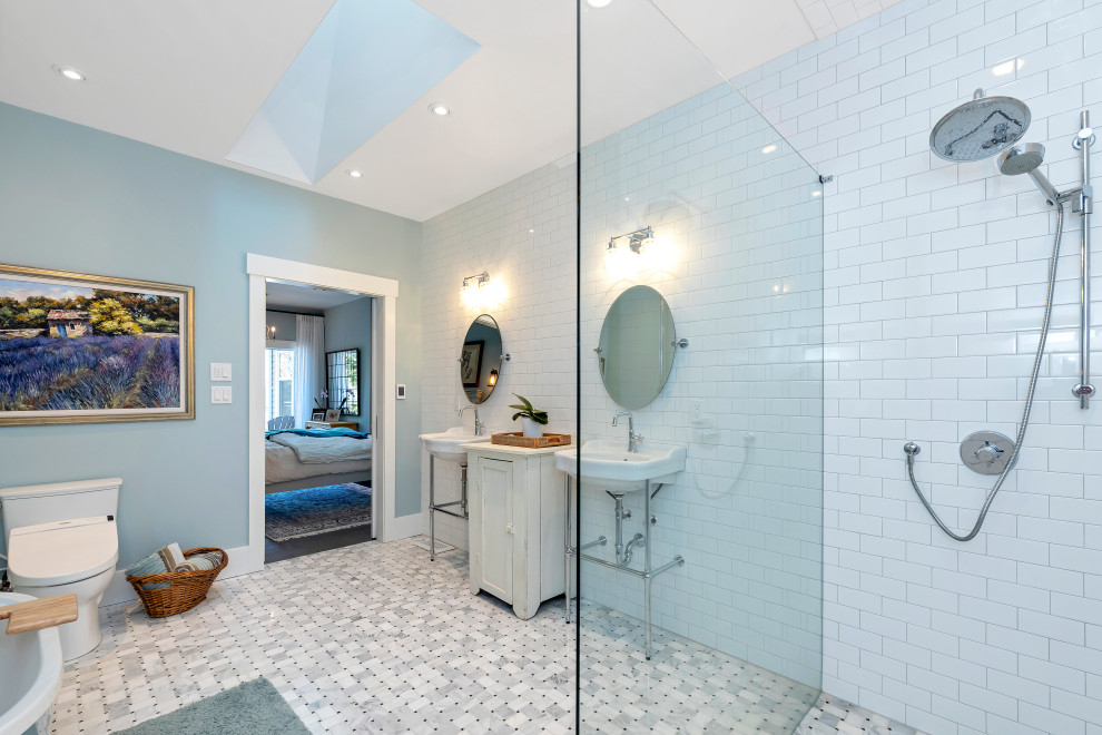 Photo of a mid-sized country master bathroom in Vancouver with open cabinets, white cabinets, a freestanding tub, a curbless shower, a bidet, white tile, subway tile, blue walls, marble floors, a pedestal sink, solid surface benchtops, multi-coloured floor, an open shower and white benchtops.