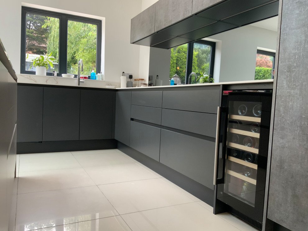 This is an example of an expansive contemporary u-shaped open plan kitchen in Buckinghamshire with flat-panel cabinets, grey cabinets, metallic splashback, mirror splashback, panelled appliances, with island and white benchtop.