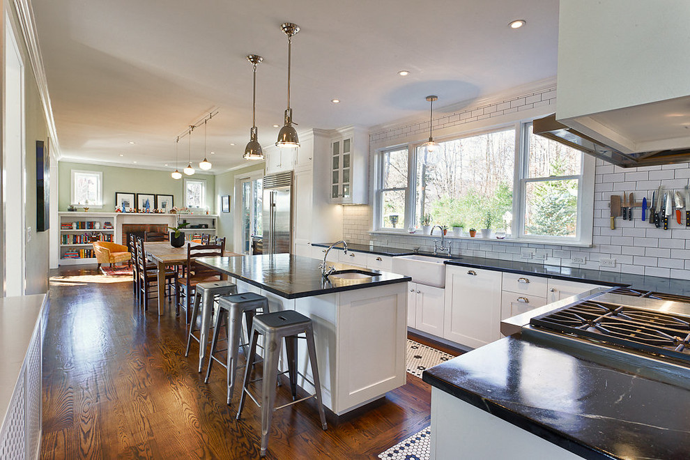 This is an example of an arts and crafts galley eat-in kitchen in New York with a farmhouse sink, shaker cabinets, white cabinets, marble benchtops, white splashback, subway tile splashback and stainless steel appliances.