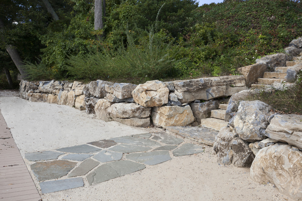 This is an example of a beach style sloped garden in New York with a retaining wall and natural stone pavers.