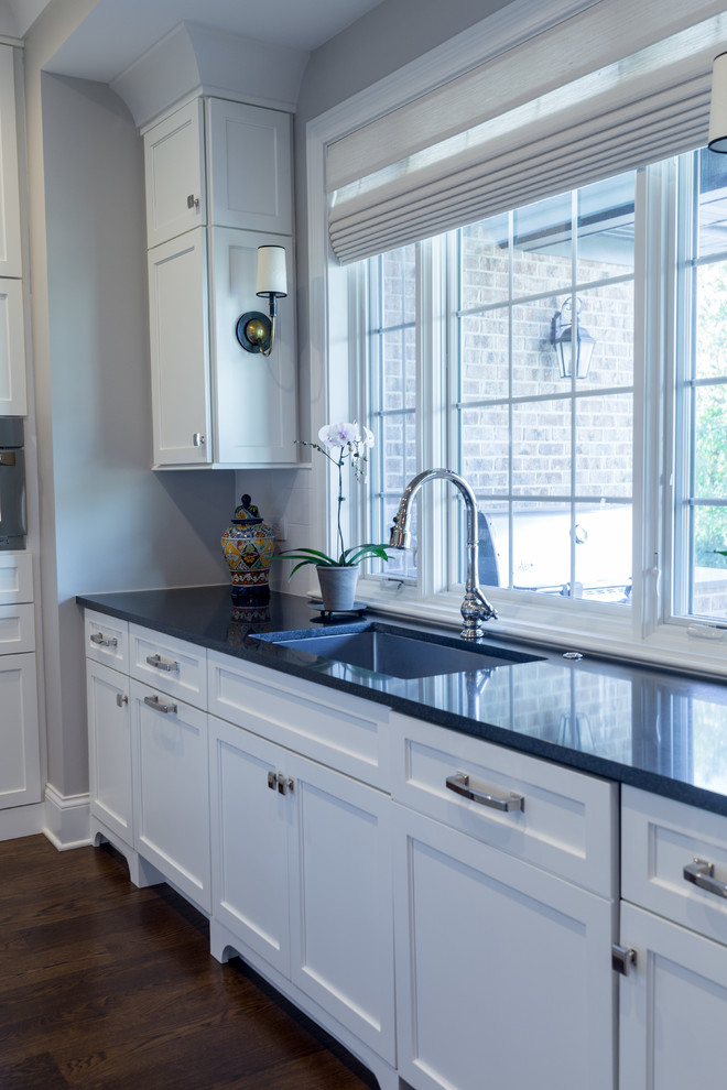 Example of a large transitional u-shaped dark wood floor and brown floor kitchen design in Chicago with an undermount sink, shaker cabinets, white cabinets, solid surface countertops, white backsplash, ceramic backsplash, stainless steel appliances, an island and black countertops