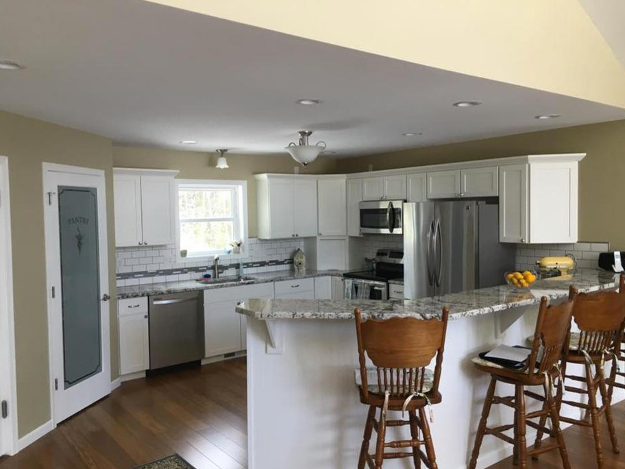 Photo of a mid-sized traditional u-shaped eat-in kitchen in Orange County with a drop-in sink, recessed-panel cabinets, white cabinets, granite benchtops, white splashback, stone tile splashback, stainless steel appliances, medium hardwood floors, no island and brown floor.