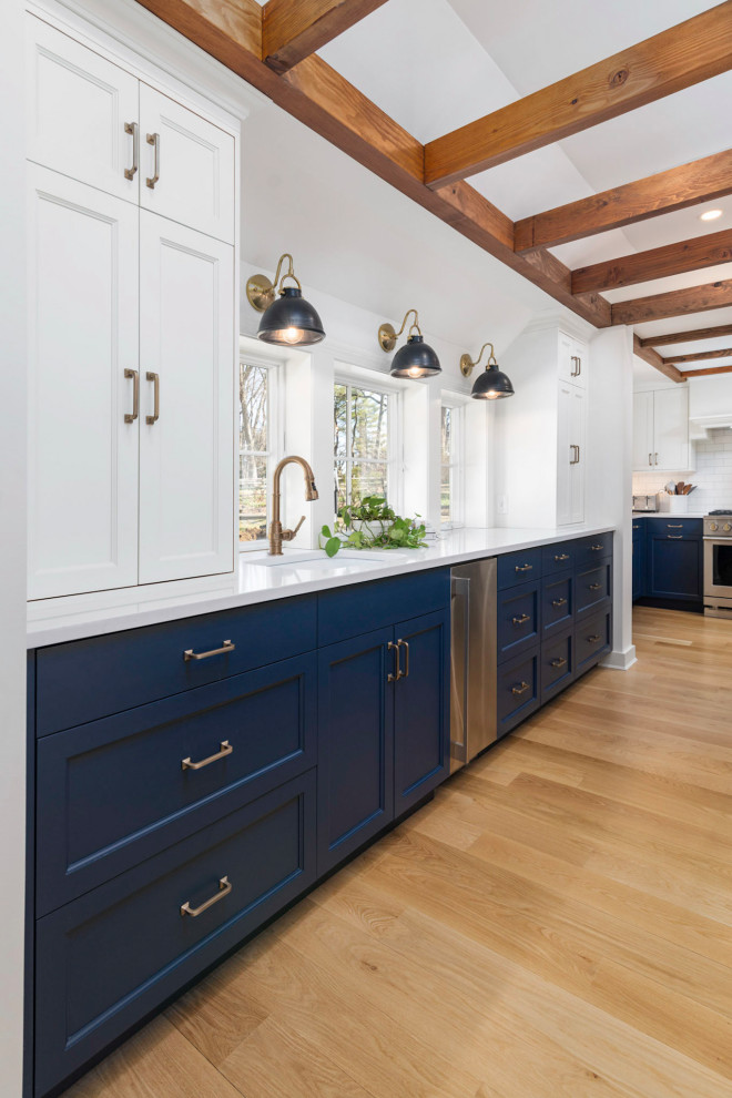 Design ideas for a mid-sized transitional l-shaped kitchen pantry in Philadelphia with a farmhouse sink, shaker cabinets, blue cabinets, quartzite benchtops, stainless steel appliances, light hardwood floors, with island, beige floor, white benchtop and wood.