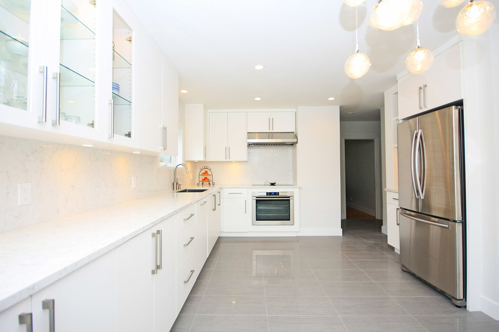 Photo of a large modern l-shaped kitchen in Vancouver with an undermount sink, flat-panel cabinets, white cabinets, quartz benchtops, white splashback, stainless steel appliances and porcelain floors.