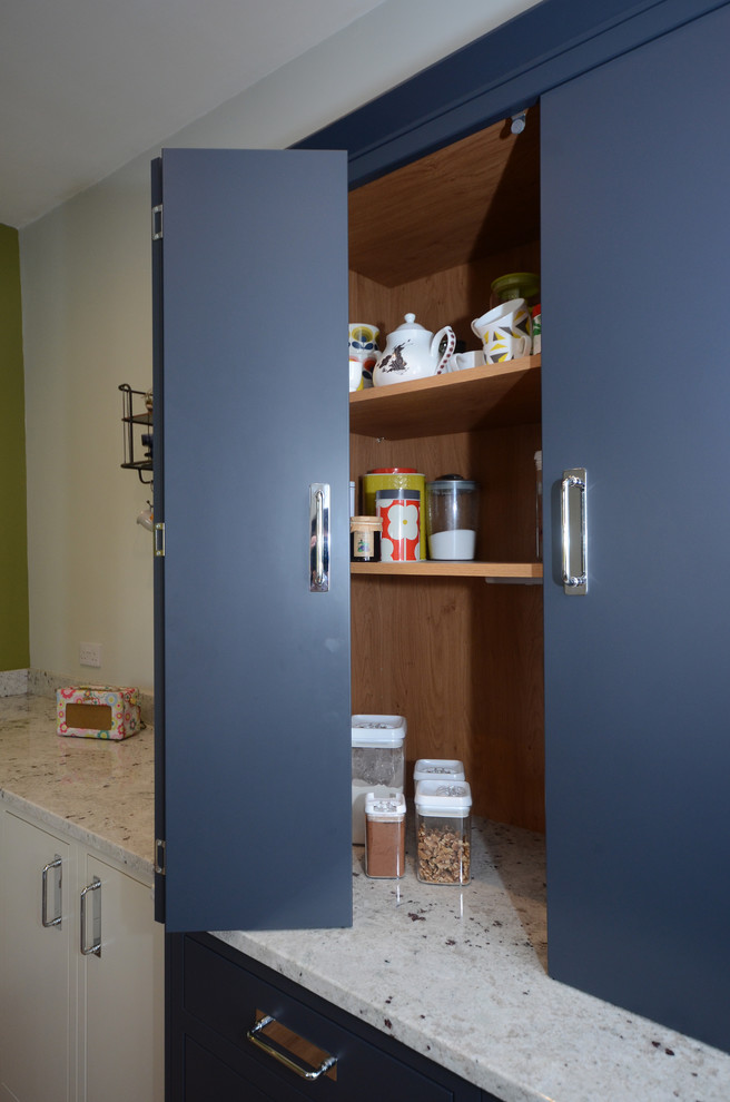 This is an example of a medium sized contemporary u-shaped enclosed kitchen with a built-in sink, flat-panel cabinets, blue cabinets, granite worktops, glass sheet splashback, integrated appliances, laminate floors, an island and white worktops.