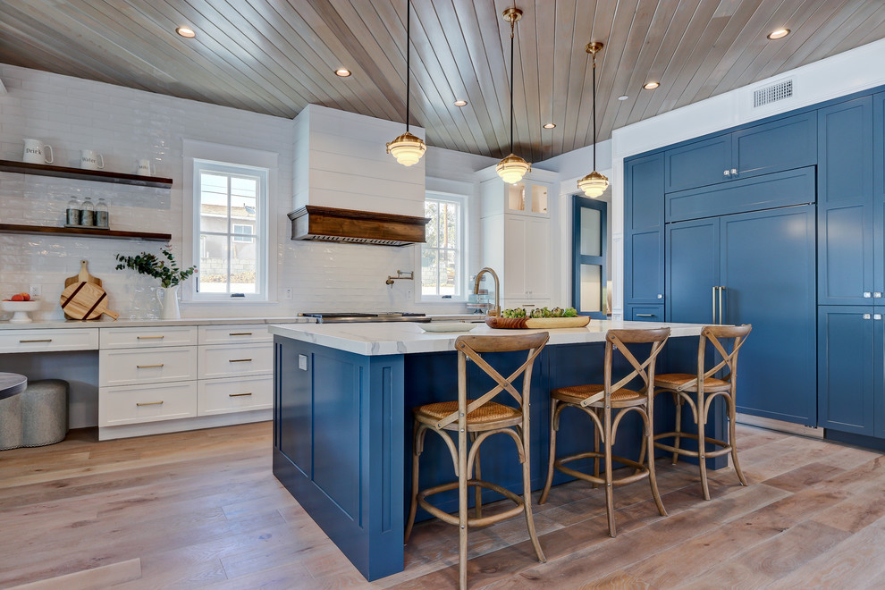 Inspiration for a beach style kitchen in Los Angeles with shaker cabinets, blue cabinets, white splashback, subway tile splashback, panelled appliances, light hardwood floors, with island, beige floor and white benchtop.