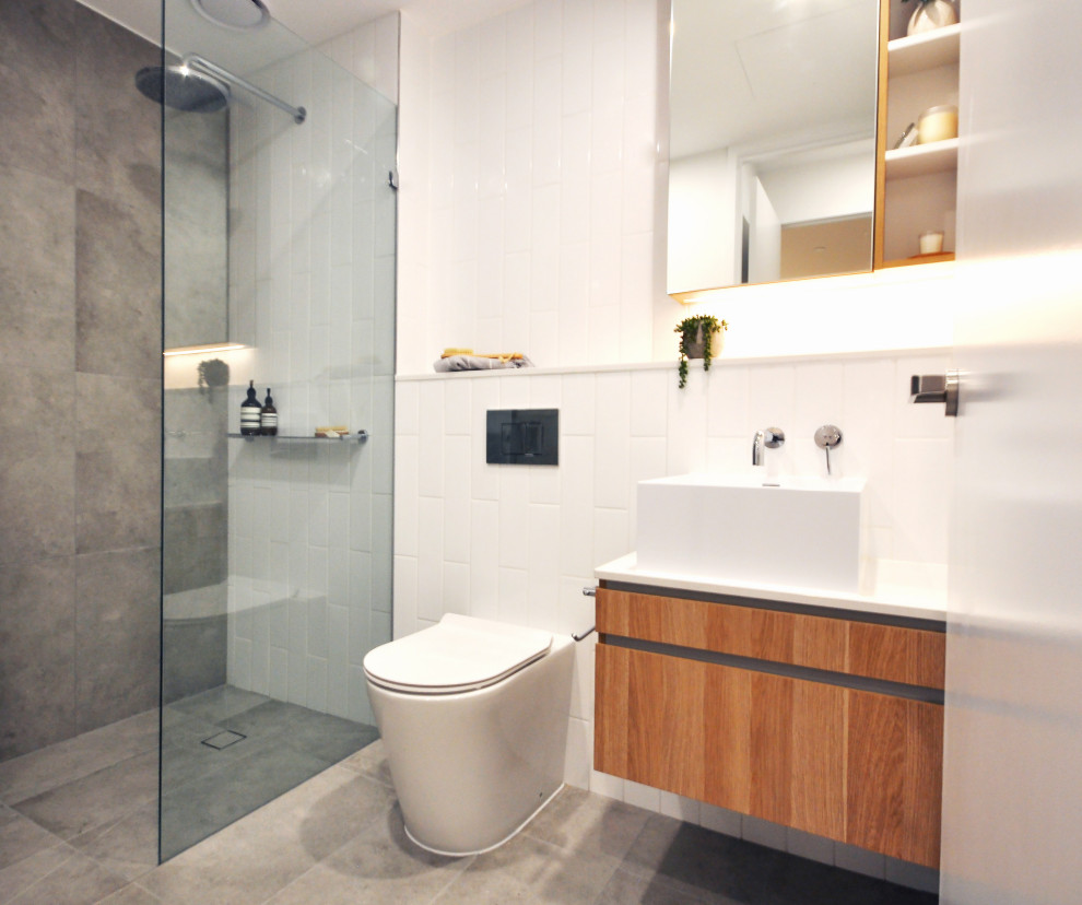 Mid-sized modern master bathroom in Melbourne with medium wood cabinets, a double shower, a one-piece toilet, white tile, ceramic tile, white walls, ceramic floors, an integrated sink, solid surface benchtops, grey floor, a hinged shower door, a single vanity, a floating vanity and wood walls.