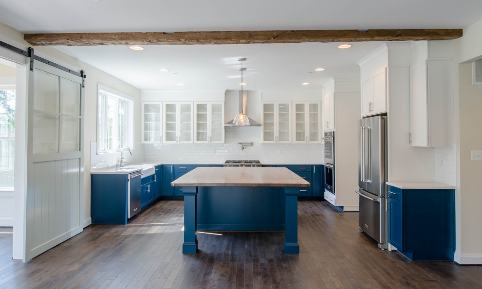 Design ideas for a country eat-in kitchen in Baltimore with a farmhouse sink, glass-front cabinets, blue cabinets, wood benchtops, white splashback, stainless steel appliances, dark hardwood floors, with island, brown floor and wood.