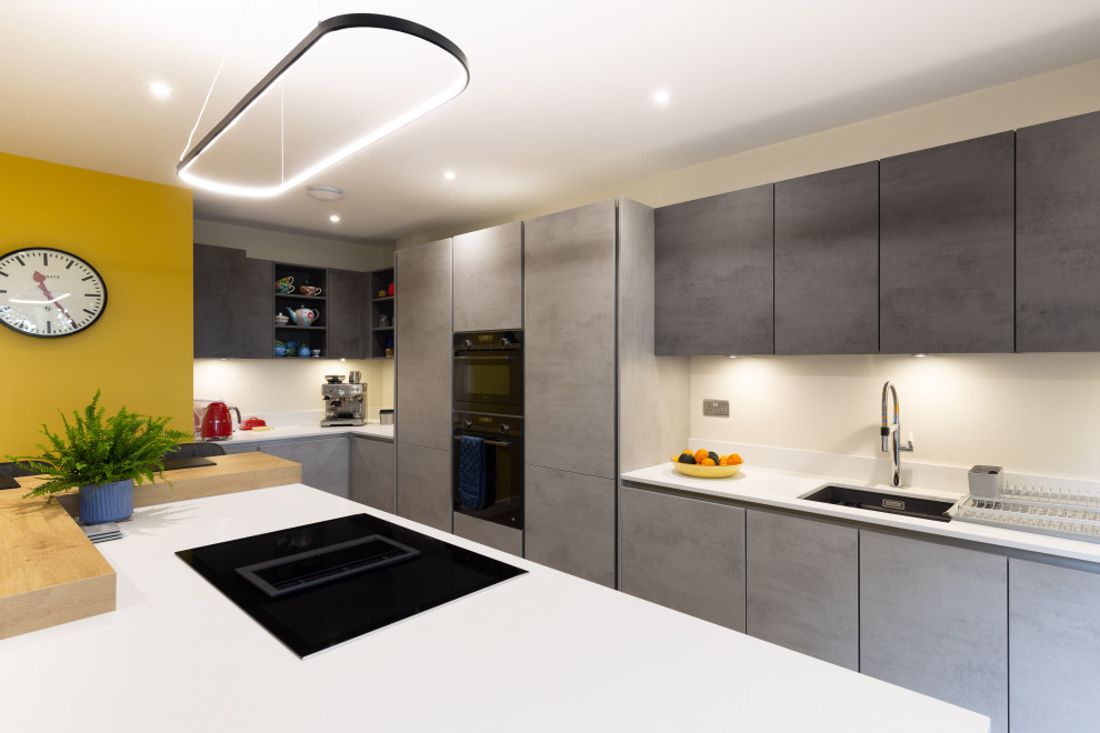 Design ideas for a mid-sized modern l-shaped eat-in kitchen in Hampshire with an undermount sink, flat-panel cabinets, grey cabinets, quartzite benchtops, black appliances, medium hardwood floors, with island and white benchtop.