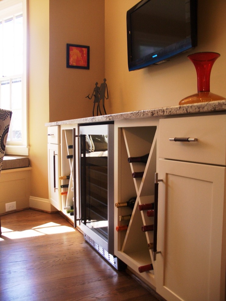 Cette photo montre une petite cuisine américaine parallèle tendance avec un placard à porte shaker, des portes de placard blanches, un plan de travail en granite, une crédence beige, un électroménager en acier inoxydable, un sol en bois brun, un sol marron et un plan de travail beige.