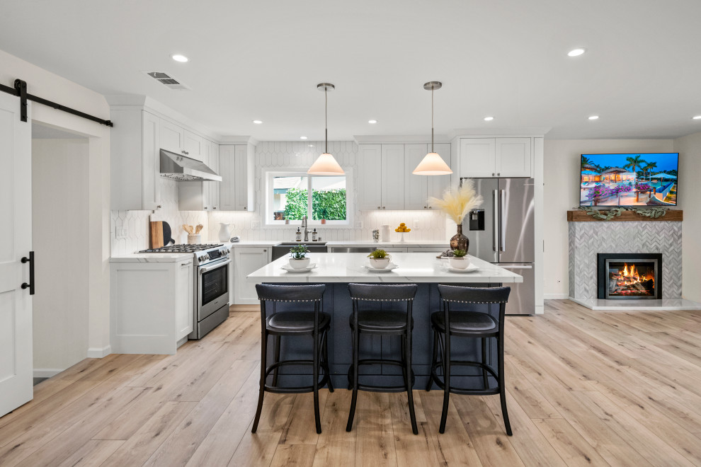 Photo of a large classic l-shaped kitchen/diner in San Francisco with a belfast sink, shaker cabinets, white cabinets, quartz worktops, white splashback, porcelain splashback, stainless steel appliances, vinyl flooring, an island, brown floors, white worktops and feature lighting.