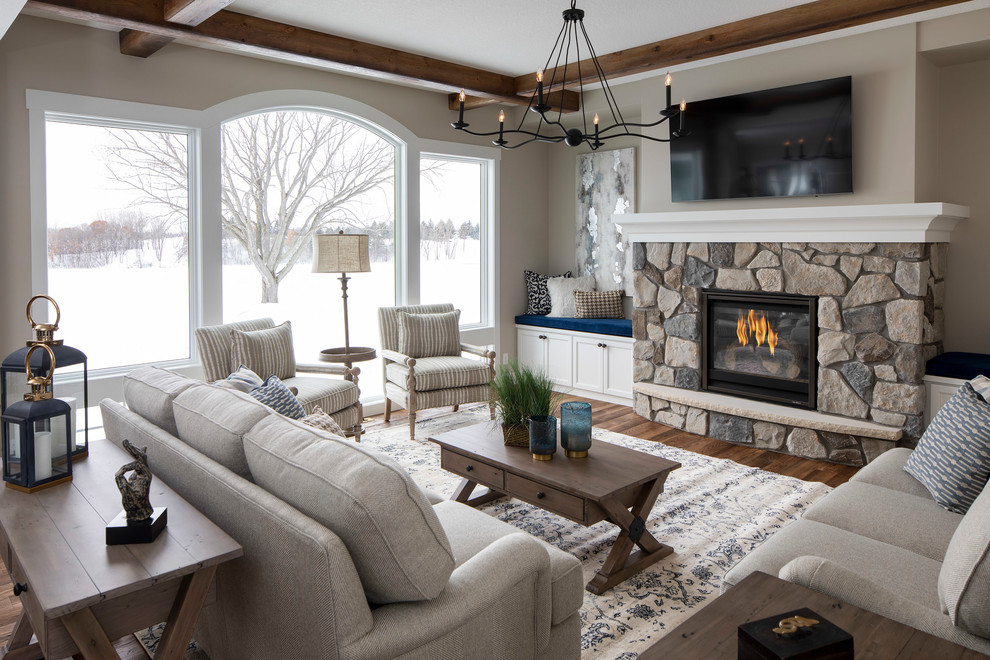 Photo of a transitional living room in Minneapolis with beige walls, medium hardwood floors, a wood stove, a stone fireplace surround, a wall-mounted tv and brown floor.