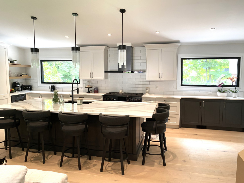 Open concept kitchen - large transitional l-shaped light wood floor and vaulted ceiling open concept kitchen idea in Toronto with an undermount sink, recessed-panel cabinets, white cabinets, quartz countertops, white backsplash, porcelain backsplash, stainless steel appliances, an island and white countertops